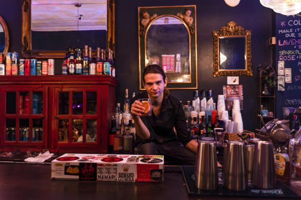 A man sits behind a bar with bottles behind him.