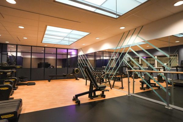 A well-lit gym with modern workout equipment, mirrored walls and geometric dividers.