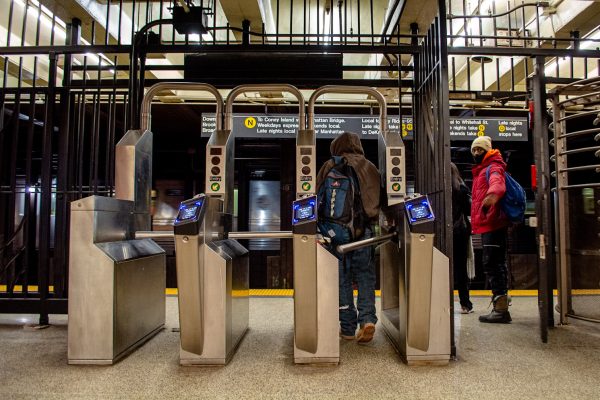 A person walks through a subway turnstile next to an open emergency exit door.