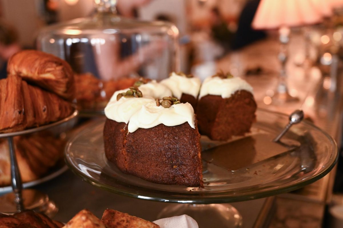 A close-up of brown cake slices topped with white frosting and green seeds, displayed on a glass platter in a bakery. (Pashmina Khan for WSN)