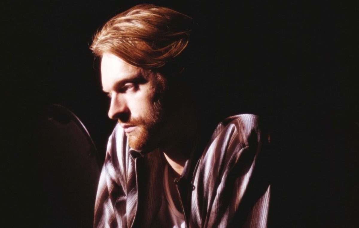 A man with long ginger hair and a beard looks away from the camera