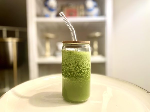 A glass jar filled with green smoothie on a white plate against a blurry kitchen background.