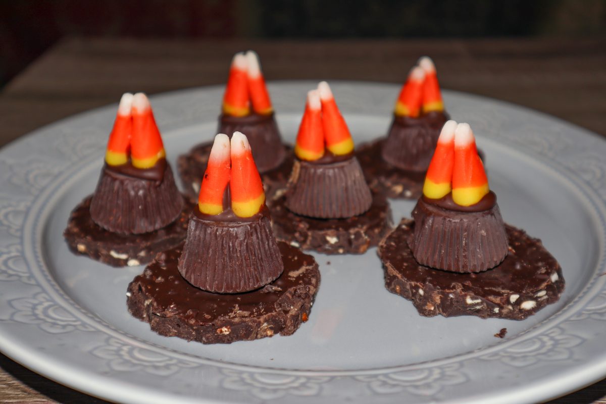 Six brown cookies on a plate with Reese's peanut butter cups and candy corn on top mimicking a witch hat.