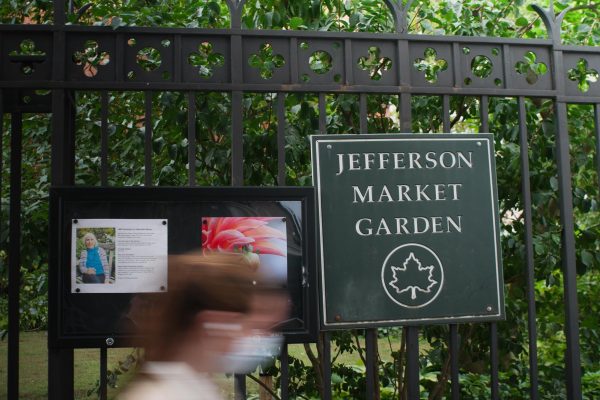  A green sign that said “JEFFERSON MARKET GARDEN" on the right and information board on the left attached to black metal fences with greenery visible behind it.