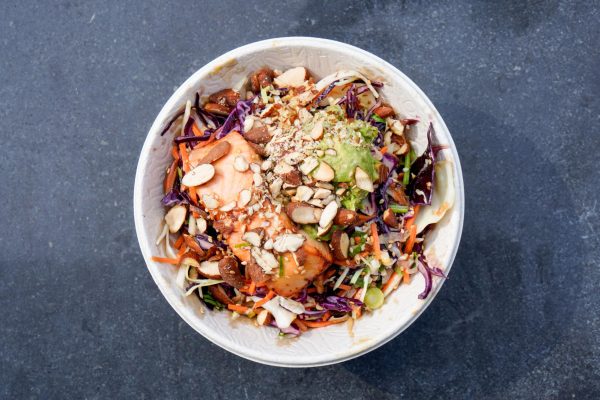 A top-down view of a bowl containing carrots, red cabbage, almond slivers and other ingredients topped with a piece of salmon and avocado.