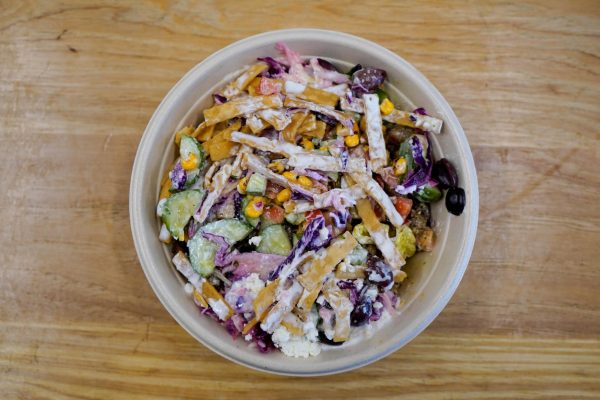 A top-down view of a circular bowl of slices of cucumber, red cabbage, corn and other ingredients all tossed in a white dressing.