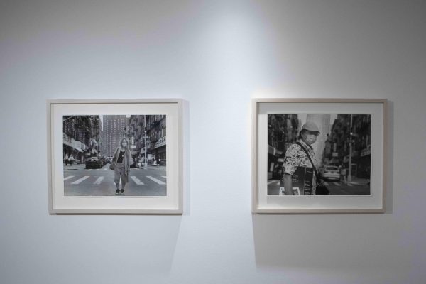  Two black-and-white photographs of people on the street hang on a gallery wall.