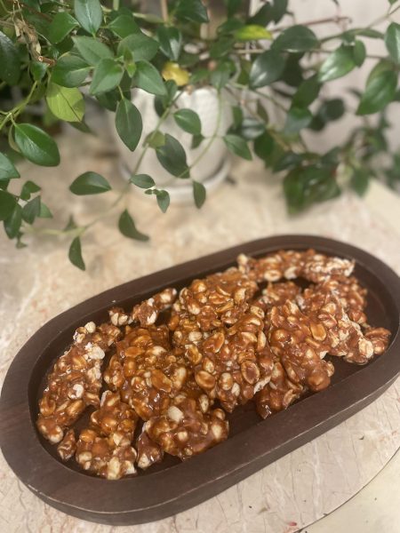 Peanuts in a brown bowl with caramel drizzled on top of them. There is a plant behind the bowl. 