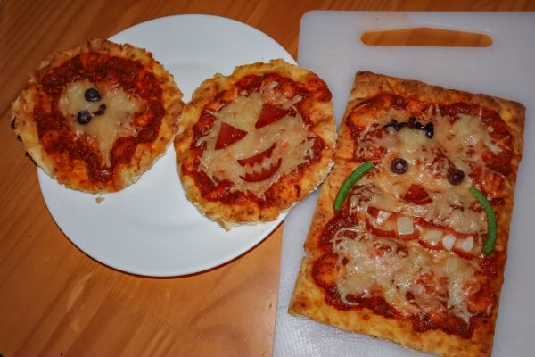 Three mini pizzas with halloween-themed faces, including a ghost, a jack-o'-lantern and a monster.