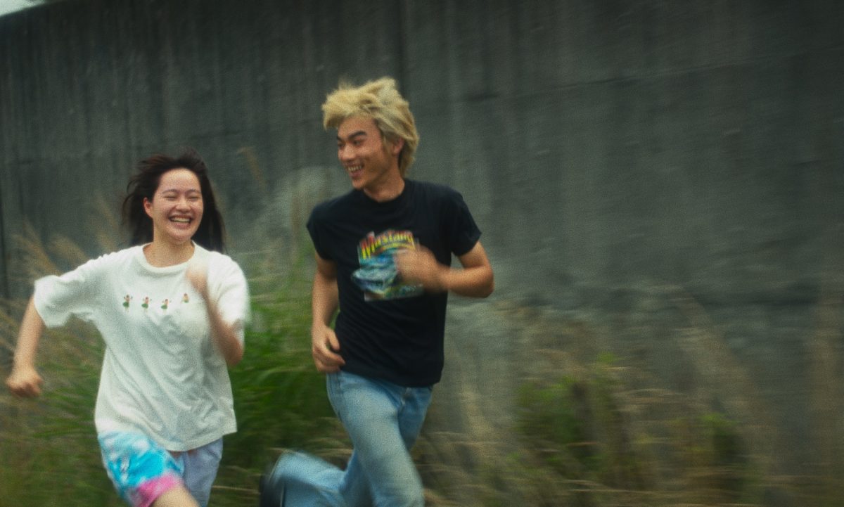 Two people run in tall grass, smiling at each other.