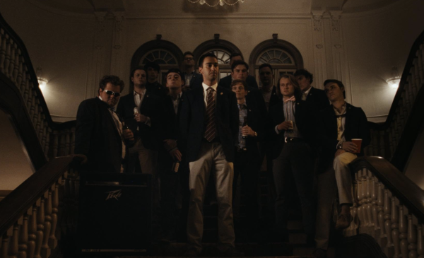 A group of men in suits and khakis stand at the top of a staircase, holding drinks.