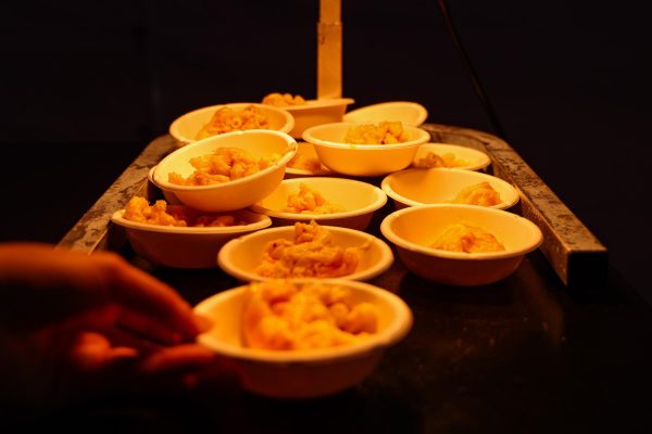 A group of bowls of macaroni and cheese under a light, with a person reaching towards one.