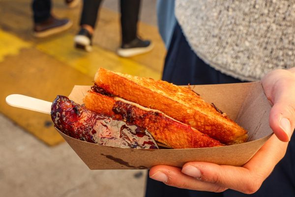 A hand holding a cardboard dish with a sandwich in it.