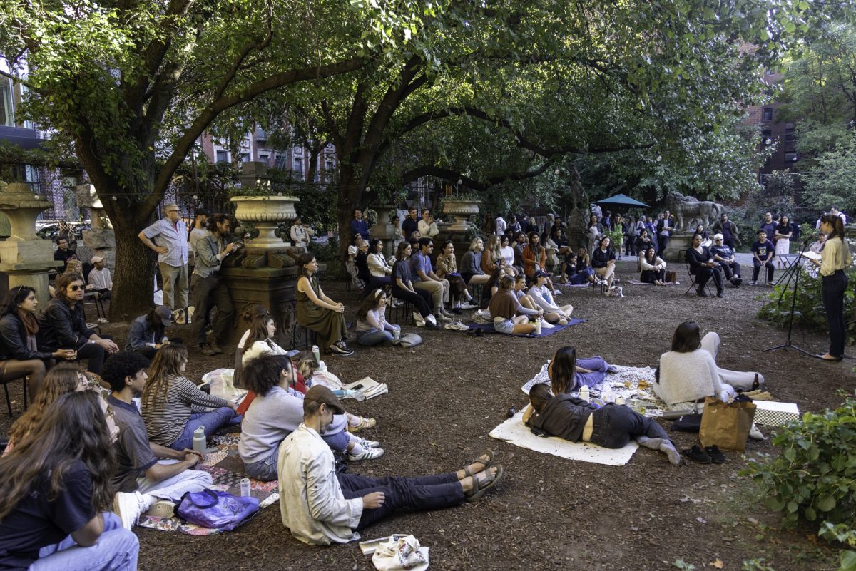 People gathering around a garden on blankets listening to a woman speak with a microphone.