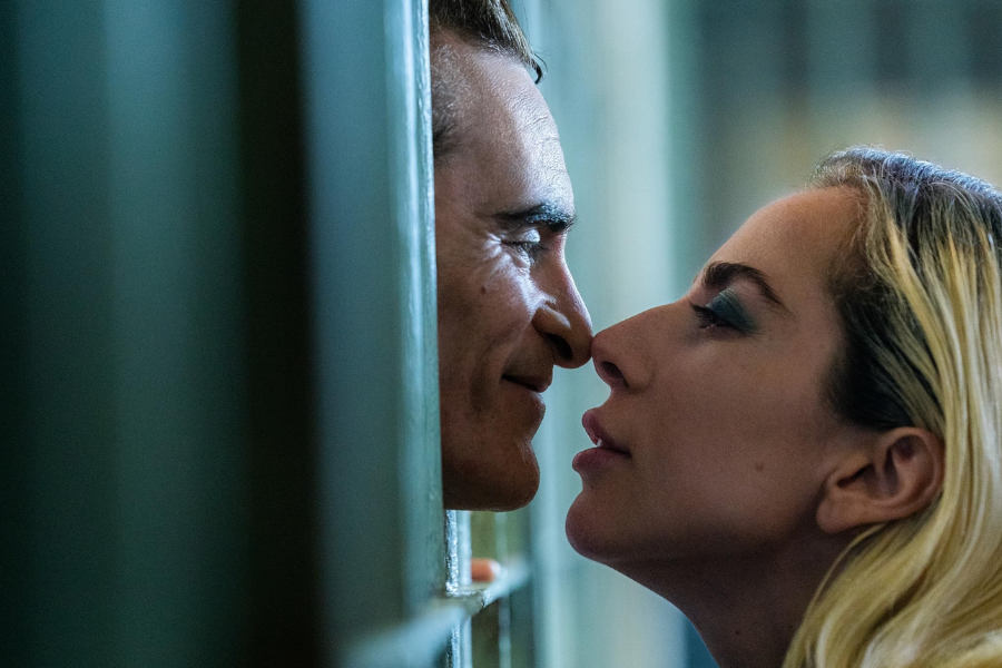 A man leans his head out through jail cell bars, touching noses with a blonde woman on the other side.