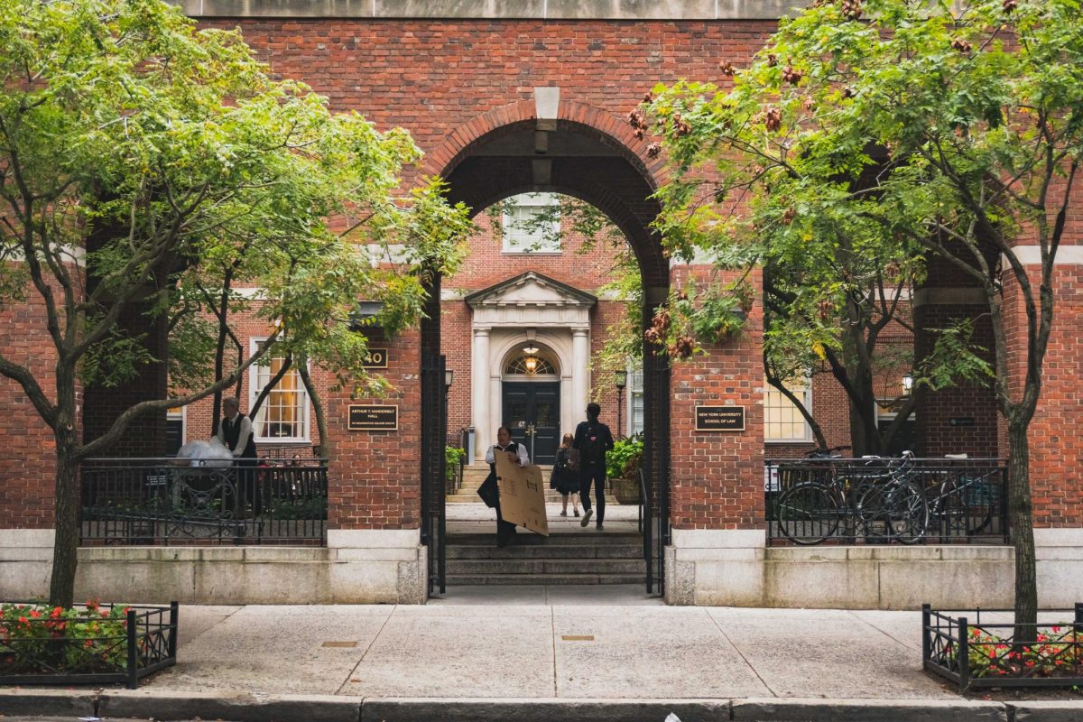 A red brick building with a large arched entrance, leading to a courtyard with people going in and out.