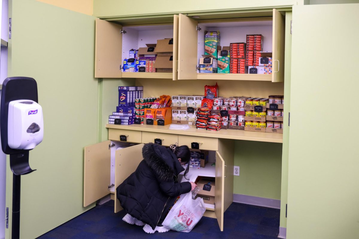 A person grabs toothpaste from a box in a drawer. The cupboards above are filled with non-perishable foods.