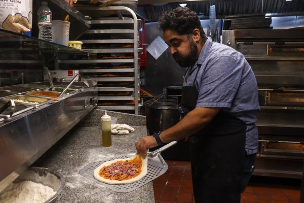 A pizza maker is placing an unbaked pizza on a pizza peel in a kitchen.