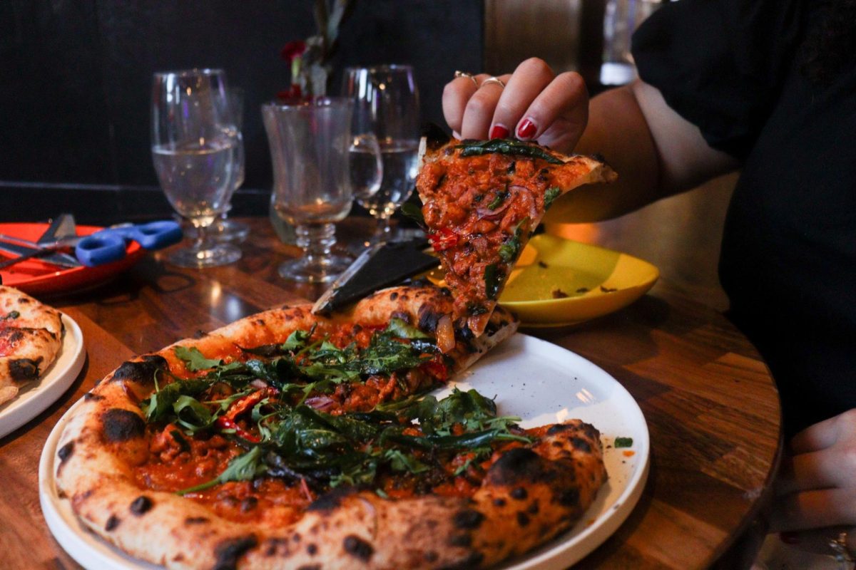 A close-up shot of a pizza with a person holding up a red pizza slice.