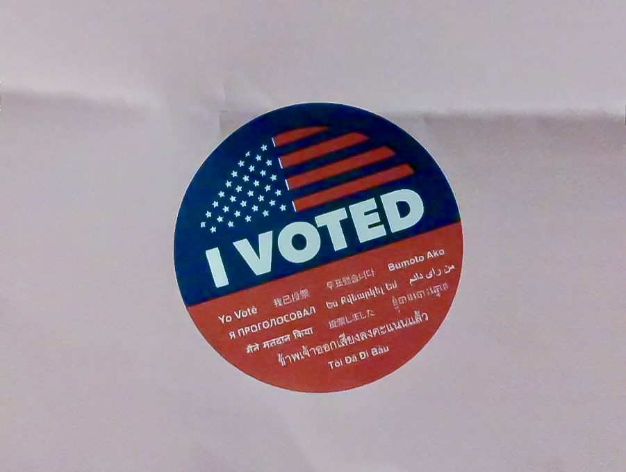 A sticker that says “I VOTED” in white text. Below the text, “I Voted” is repeated in 12 different languages.