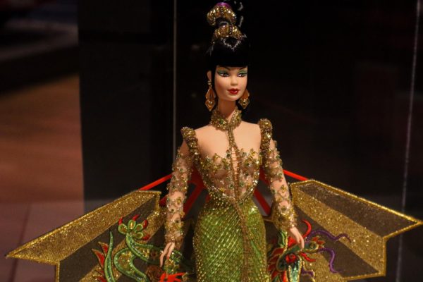 A black-haired Barbie doll wearing a green and gold beaded dress and a gold cape with a green dragon design.