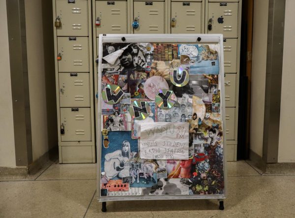 A poster covered in stickers reads “W.N.Y.U.” in front of a wall of lockers.