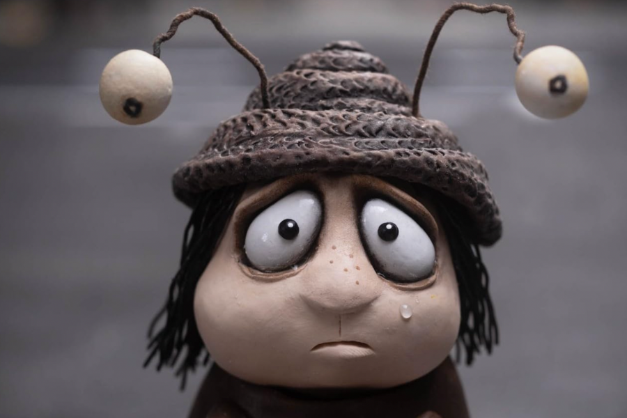 A sad Claymation figure with wide, teary eyes wearing a textured hat and snail-eyes headpiece.