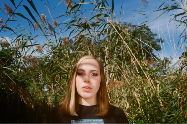 A film photo of a woman standing in a field surrounded by tall plants.