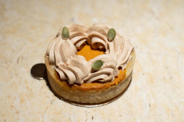 A round pastry with off-white frosting and dark green seeds on top.