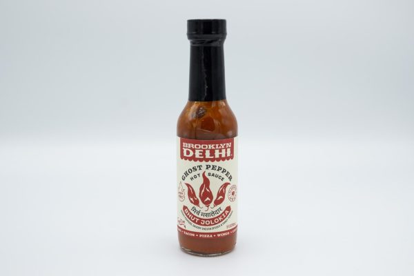 A bottle of red hot sauce with a white and red label that reads “Brooklyn Delhi, Ghost Pepper Hot Sauce” with a logo of three peppers designed to look like flames below.