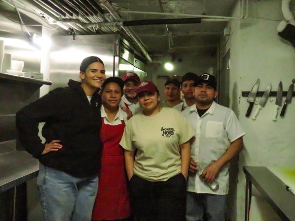 A group of people stand smiling at the camera in the middle of a kitchen.