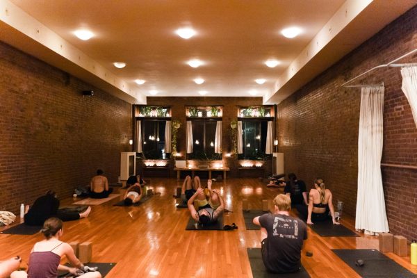 People lay on mats in various poses inside of a yoga studio.