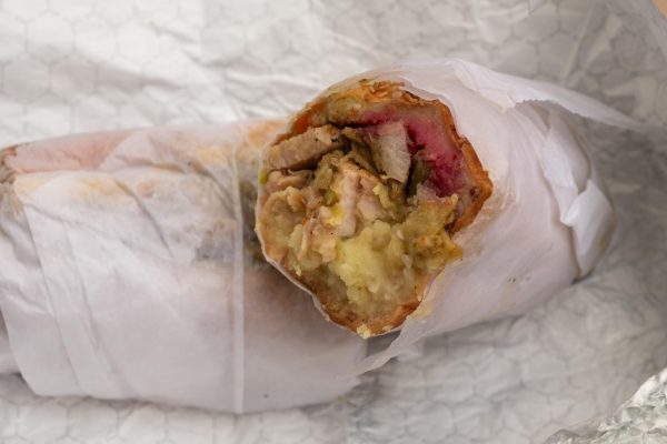 A sandwich filled with turkey, mashed potatoes, greens and cranberry sauce wrapped in paper and sitting in an aluminum wrap.