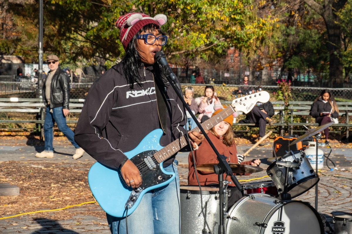 A woman wearing mouse ears playing guitar and singing in a park.