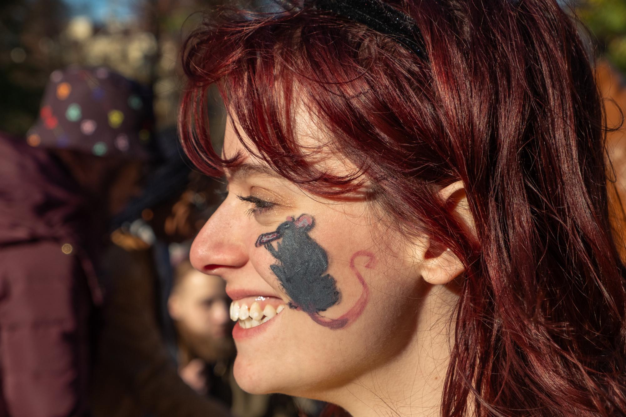 A woman smiling with a rat painted on her cheek.