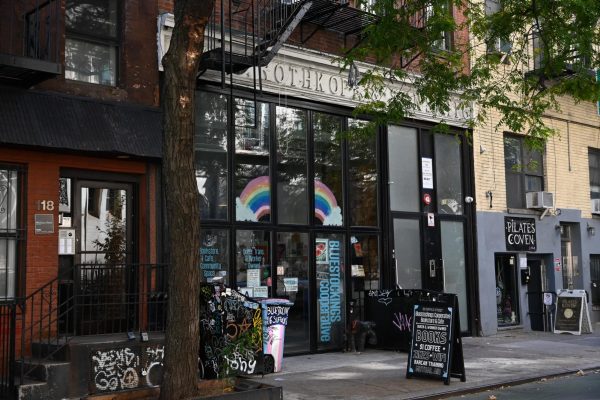 A storefront with a rainbow and "BLUESTOCKINGS COOPERATIVE" written in blue text painted on the glass door.