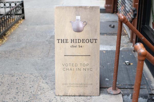 A sign on the sidewalk that reads “THE HIDEOUT” and “chai bar” under a graphic of a teapot. Underneath is the message “VOTED TOP CHAI IN N.Y.C.”