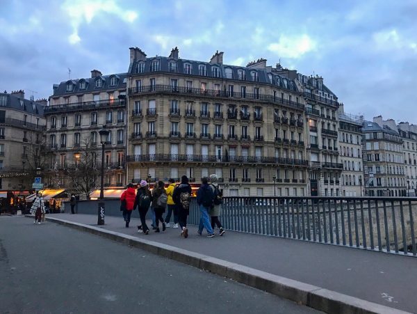 Students are walking down a street by N.Y.U. Paris at night.