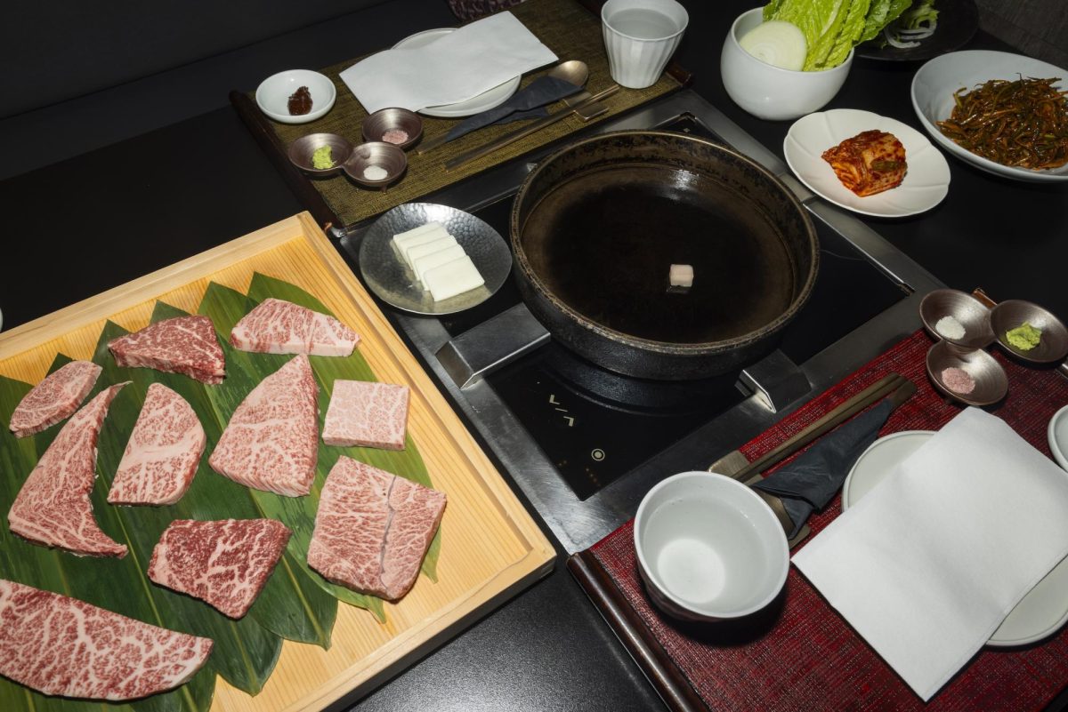 A hot pot layout of food, containing several uncooked pieces of beef, butter, vegetables, spices and a heated pan for cooking.