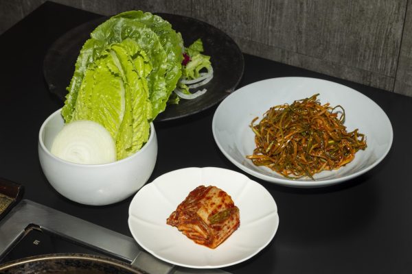 Several side dishes including lettuce, onion, kimchi and stir-fried vegetables rest on a table.