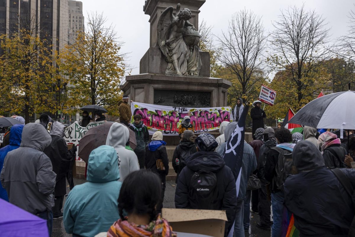 Protestors stand in front of a statue with a banner under it that reads “The Student Intifada.”