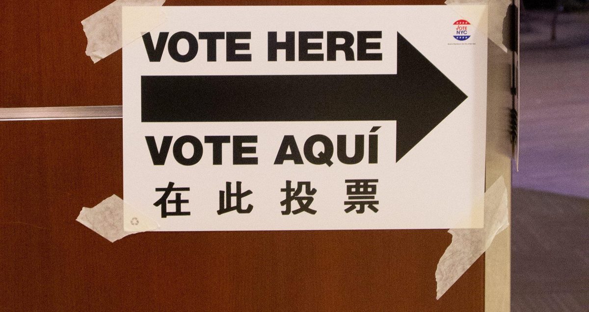 A sign that reads “VOTE HERE” and “VOTE AQUI” with a black arrow pointing towards a door.