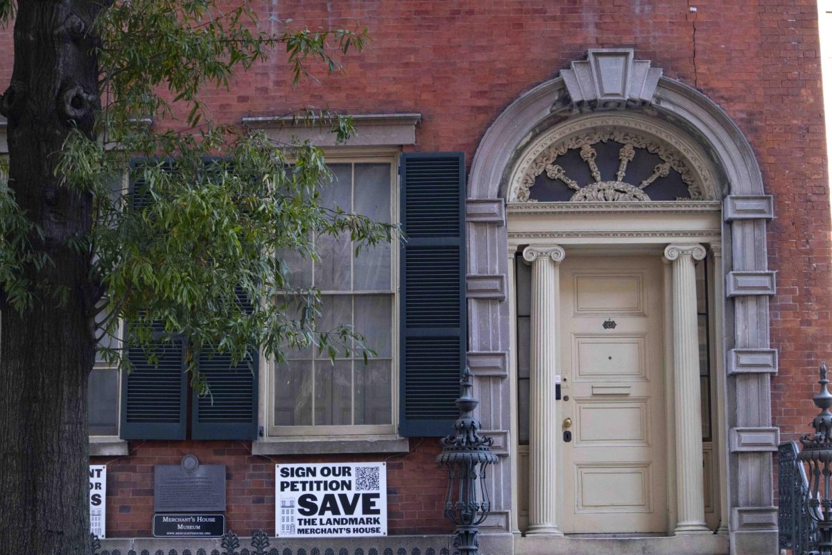 The front of a brick building with a white door. There is a sign to the right of the door that reads “SIGN OUR PETITION SAVE THE LANDMARK MERCHANT’S HOUSE”