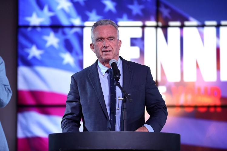 Robert F. Kennedy Jr. talking at a podium with a screen of the American flag behind him.