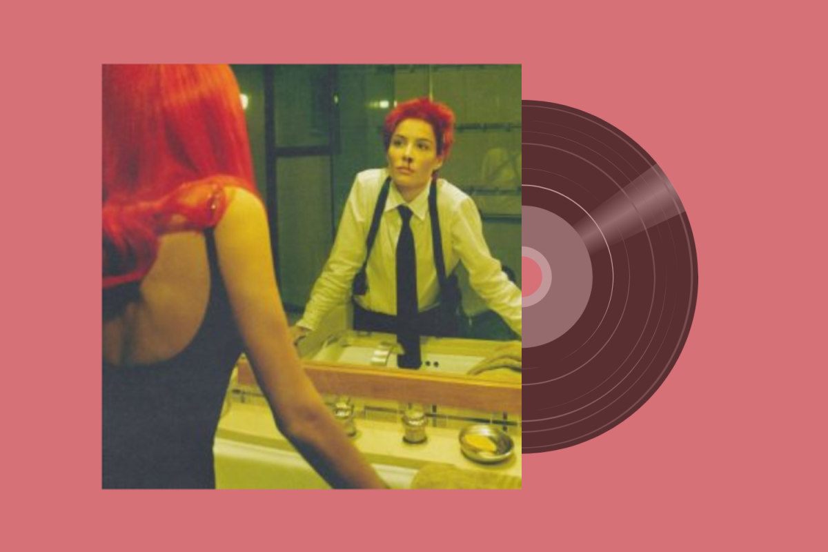 A person looking into the mirror over a sink with striking red hair and a bloody nose. There is a record coming out behind the photo.