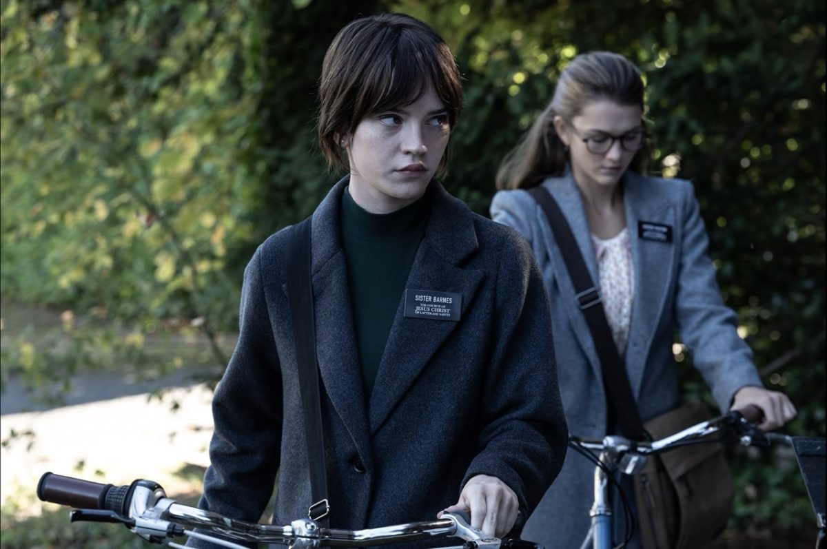 A girl dressed in black with a name tag that reads “Sister Barnes.” Behind her is a girl dressed in gray.