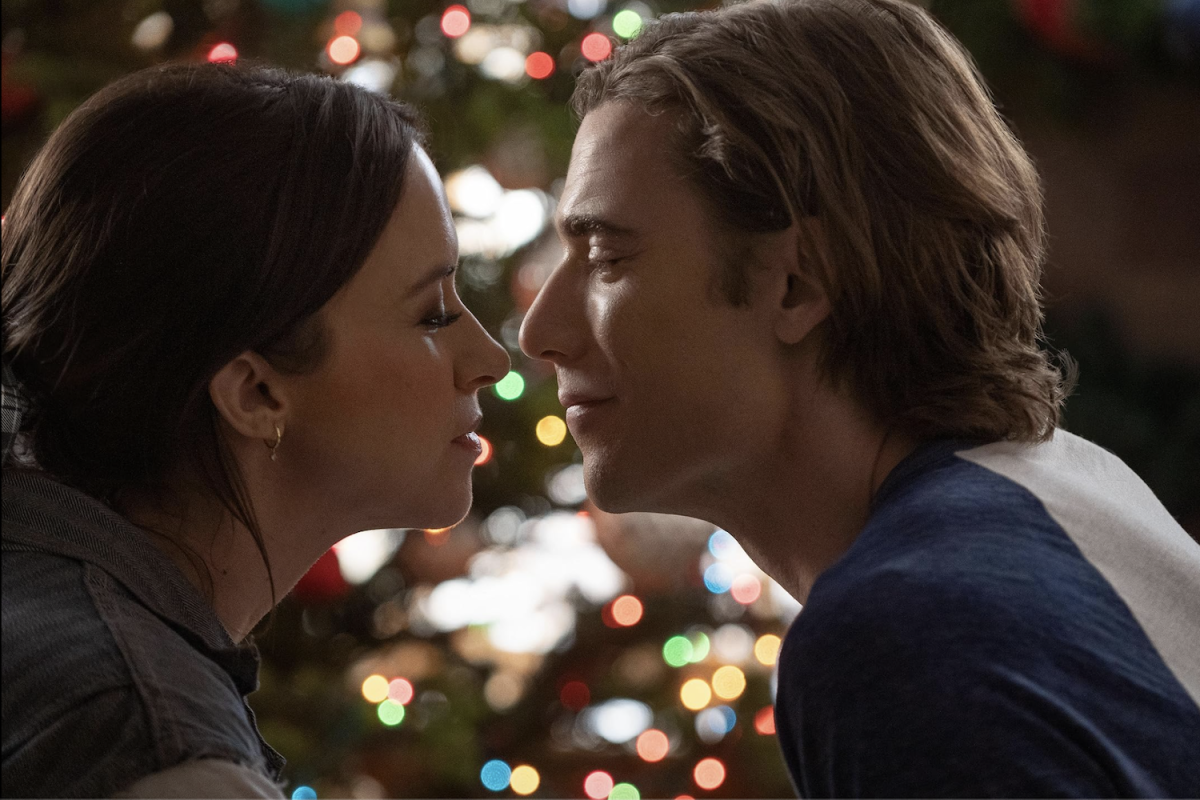 A man and a woman lean towards each other with a Christmas tree behind them.