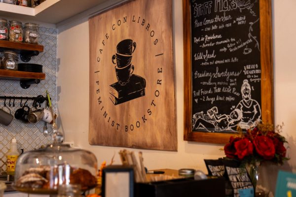 A wooden sign of Café con Libros hangs above a coffee counter on the interior wall of a shop