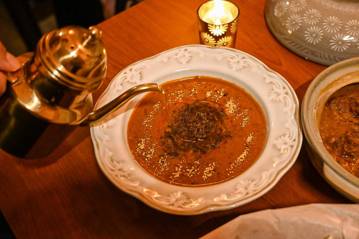 A golden teapot pouring a clear liquid over a dish of orange soup.