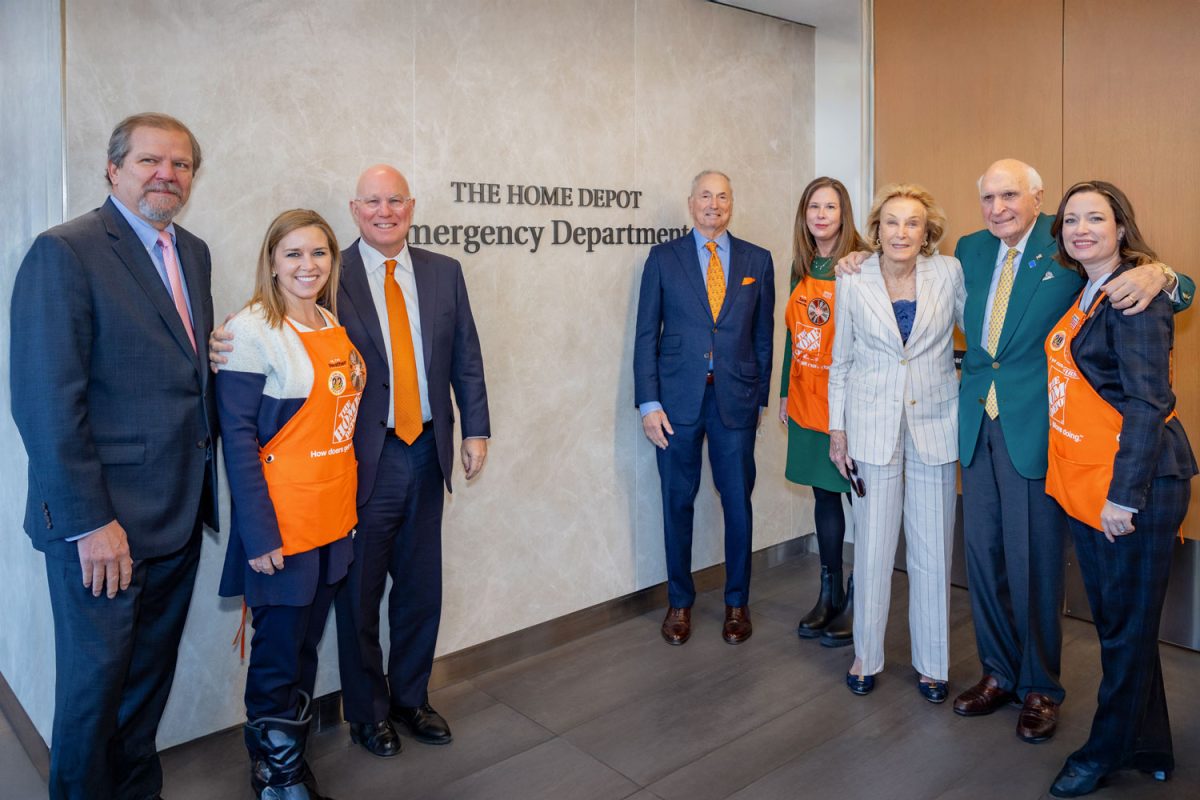 People in suits stand against a wall reading "THE HOME DEPOT Emergency Department."